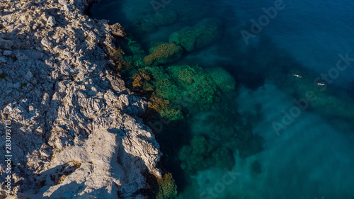 Blue Water and Rocky Beach, Top Down View, People Swim in Sea