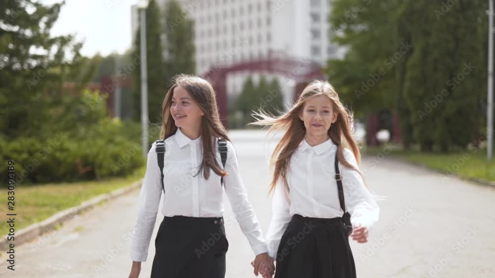 Two schoolgirls walk together holding hands, pullback shot with copy space
