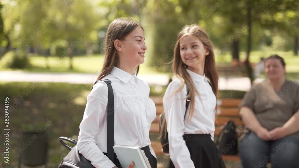 Two young happy school girls walk together through park Two young happy school girls walk together through park