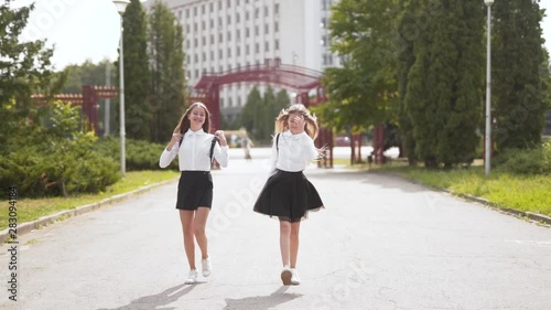 Happy go lucky schoolgirl walk and dance on path together holding hands