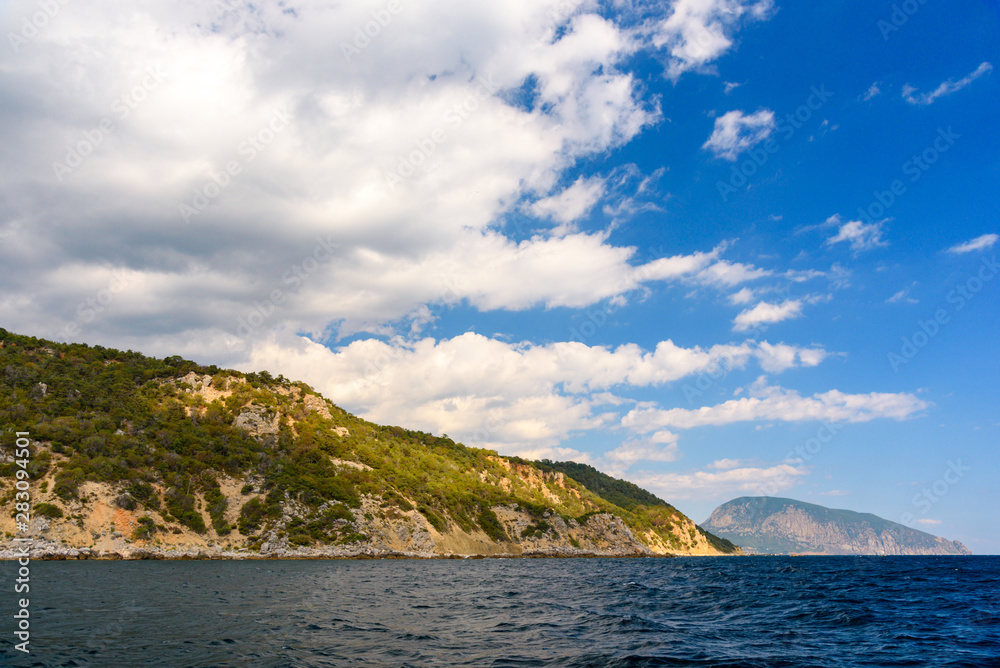 Ayu-Dag mountain from the side of a pleasure boat in the black sea, on a sunny day with clouds in the sky.