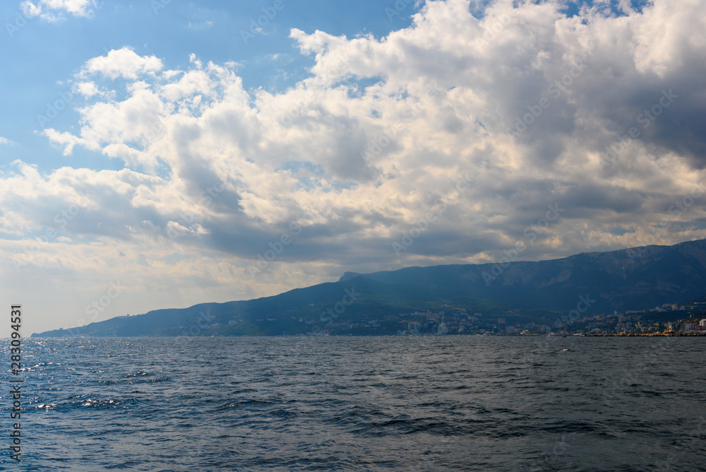 The resort city of Yalta from the side of a pleasure boat in the black sea, on a sunny day with clouds in the sky.
