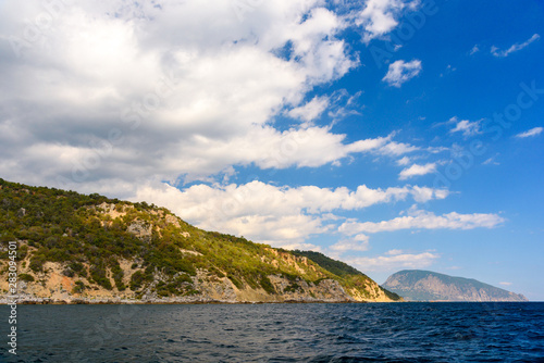 Ayu-Dag mountain from the side of a pleasure boat in the black sea, on a sunny day with clouds in the sky. © StockAleksey