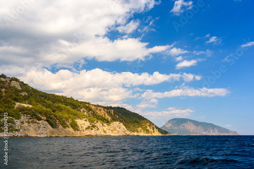 Ayu-Dag mountain from the side of a pleasure boat in the black sea, on a sunny day with clouds in the sky.