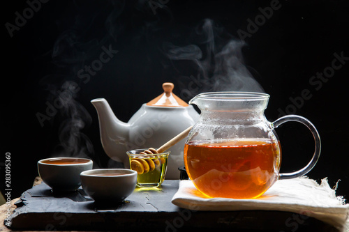 Hot tea in a teapot and teacup with steam on revive the wood and a black background.
