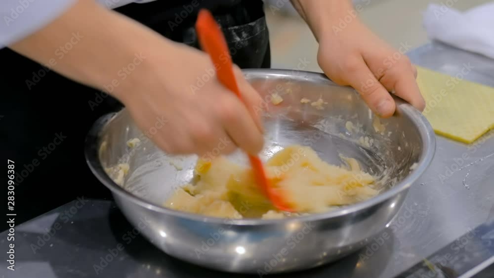Close up shot - chef hands kneading fresh dough with spatula in iron bowl on the kitchen table at cuisine of restaurant. Professional cooking, catering, bakery, gastronomy and food concept Close up shot - chef hands kneading fresh dough with spatula in iron bowl on the kitchen table at cuisine of restaurant. Professional cooking, catering, bakery, gastronomy and food concept