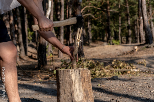 A man chopping wood on a stump in the forest on a sunny summer day. Travel and camping