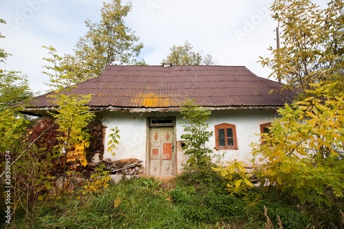 shabby and old country house, made of wood and clay, against cloudy October sky, open yard, desolation and autumn depression concept © Valeronio
