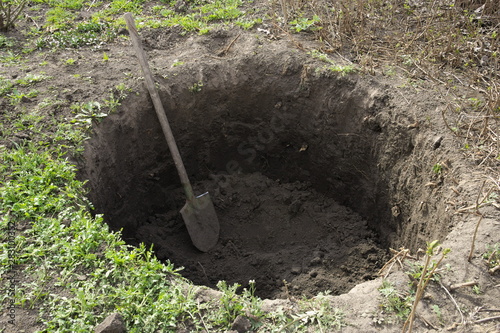 Deep pit in the ground. In the pit lies a shovel. Digging a hole.
