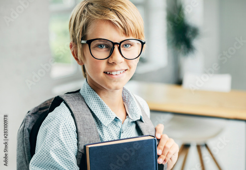 Smiling blond boy holding books in a classroom