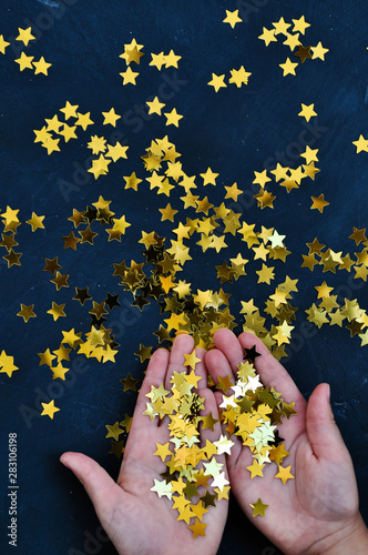 Baby hands holding shiny gold star confetti on a dark background in anticipation of Christmas and New year.