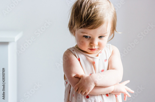 Sad toddler baby girl looking down with her arms crossed