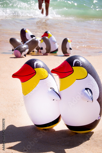 two blow up penguins on a sandy beach with a group blow up peguins behind photo