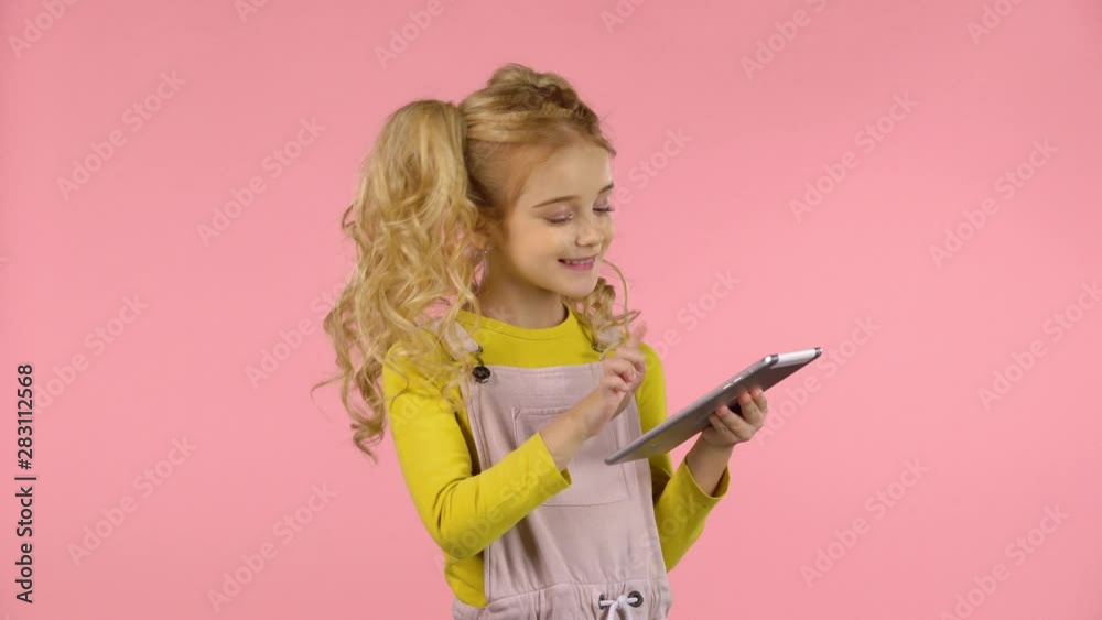 Pretty little female child is playing with the tablet and sending a blow kiss.