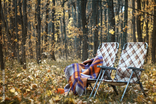 Two folding sun loungers and a warm woolen plaid in the forest in autumn among the fallen foliage, a cozy autumn concept, selective focus