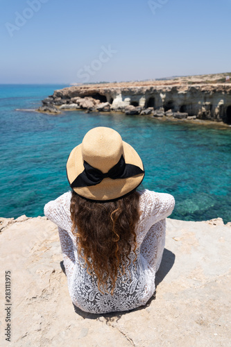 Model with a wide brim straw summer hat on the edge of Cape Greco (Cavo Greco, Capo Greco). Concept of high end summer vacation, vintage style summer look.