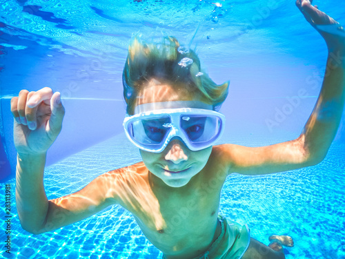 Underwater view of a young boy having fun into the swimming pool. Happy teenager with scuba mask. Tourist teen enjoying summer holiday playing in the water. Youth, summer vacation happiness concept