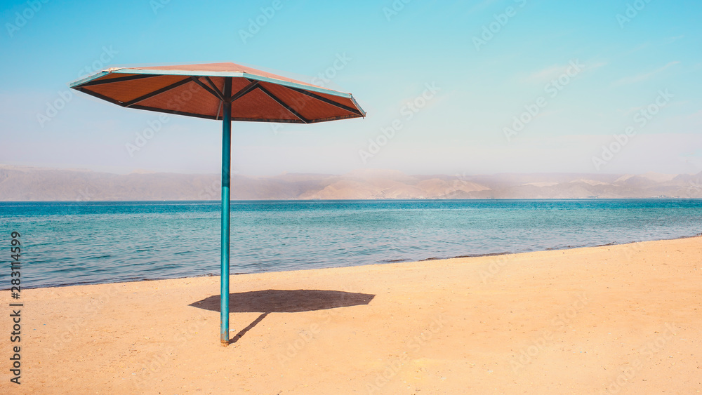 Beach side rest chairs and umbrellas on the sand near the blue water and horizon