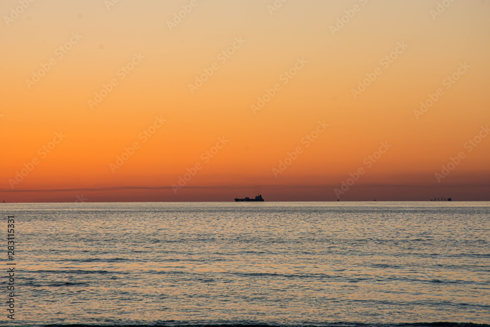 Beautiful orange sky sunset view with ship silhouette in uae beach