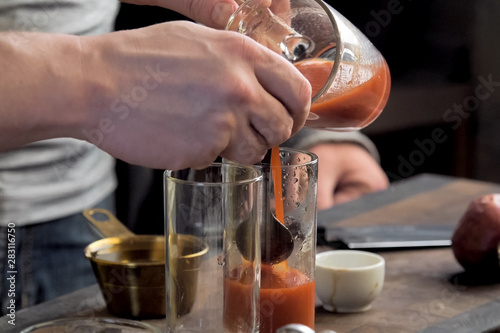 Pouring tomato juice into glasses through spoon.