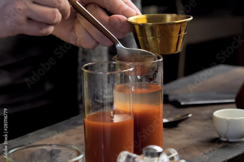 Pouring tomato juice into glasses through spoon.