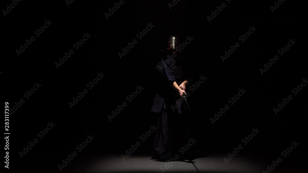 Kendo fighter performing martial art with Katana sword at dark studio under spotlight. Kendo fighter performing martial art with Katana sword at dark studio under spotlight.