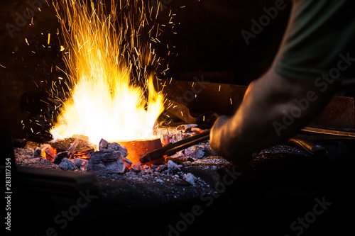 Unrecognizable Hands of Smith Preparing Metal on Anvil for Forging with spark fireworks