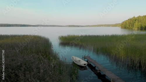Aerial, static, drone shot, of a rowboat, at a wharf, surrounded by reed, in calm waters of lake Hvittrask, on a sunny, summer day, in Kirkkonummi, Uusimaa, Finland photo