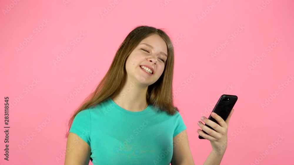 Girl talking at video chatting on cell phone in studio against pink background. Girl talking at video chatting on cell phone in studio against pink background.