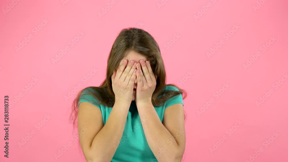 Little female is scared and hiding her face in studio on pink background. Little female is scared and hiding her face in studio on pink background.