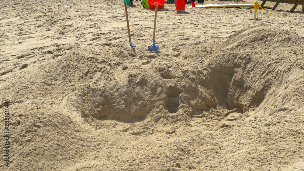 Two shovels are seen standing in the sand that where used by kids to dig a big hole in the sand. 