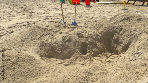 Two shovels are seen standing in the sand that where used by kids to dig a big hole in the sand. 