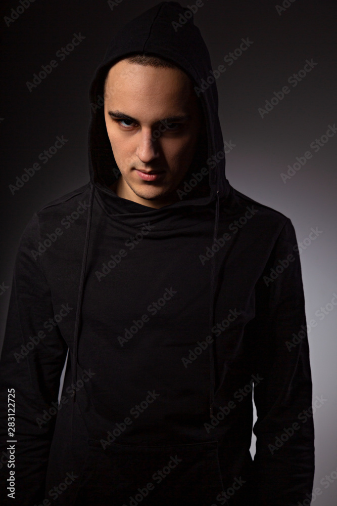 Mysterious serious man in black hoodie with hood on the head on dark background. Dangerous criminal person