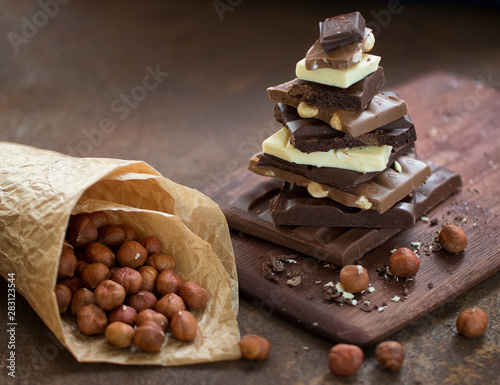 Obraz na plátne The different grades of chocolate put by the hill on a wooden board, with a filbert in a paper package on a rusty metal surface