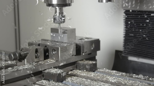 SLOW MOTION, CLOSE UP: Shiny chips fly off a piece of aluminium being processed by a CNC drill. Conventional fine end mill drill cutting and shaving a small block of metal into an unfinished product. photo