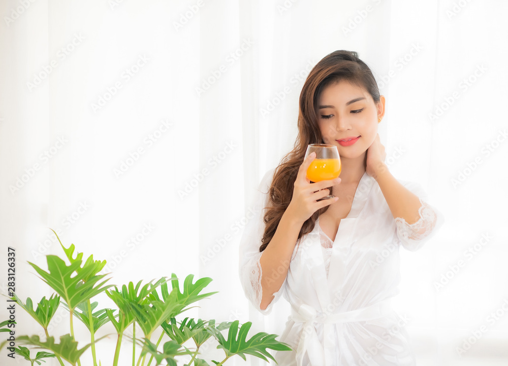 Portrait of a cute woman with brunet hair wearing white dress isolated over white background , drinking orange juice cocktail from a glass.