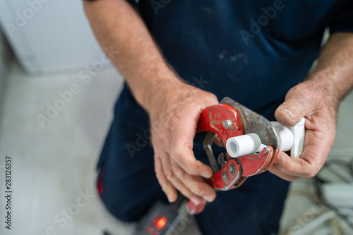 Close up on hands of plumber cutting plastic pipes cut white plumbing installation craftsman at work