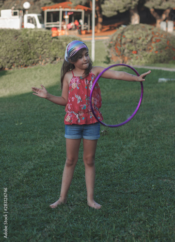 Little girl is playing with her hula hoop in the park 