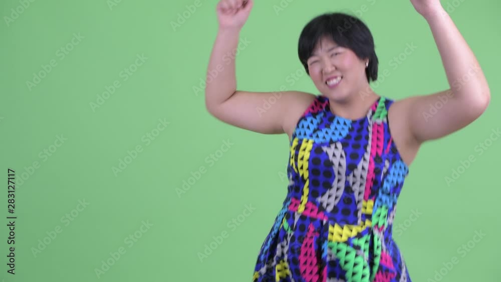 Happy young overweight Asian woman touching something and dancing Happy young overweight Asian woman touching something and dancing