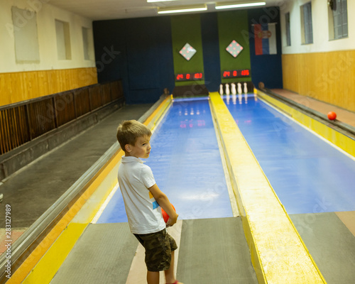 The little boy photographed from behind is sitting in a bowling alley photo