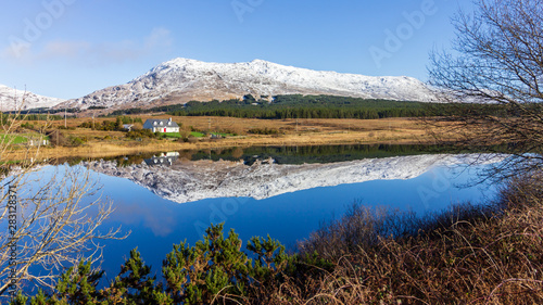 A lake in Connemara  Galway County  Ireland reflects houses  a mountain and sky on a sunny day