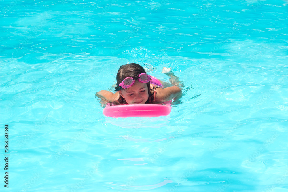 Cute Little girl practices swimming on a kick board in the pool