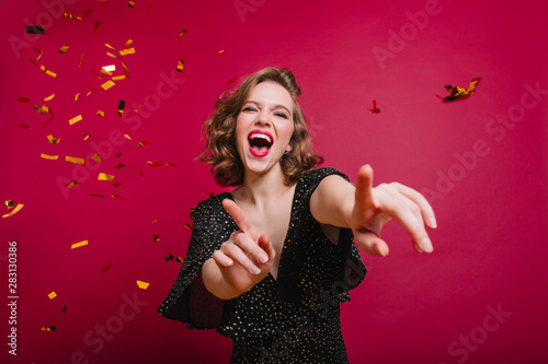 Inspired short-haired fun lady dancing under sparkle confetti and laughing. Ecstatic caucasian female model in vintage black attire spending time at new year party.