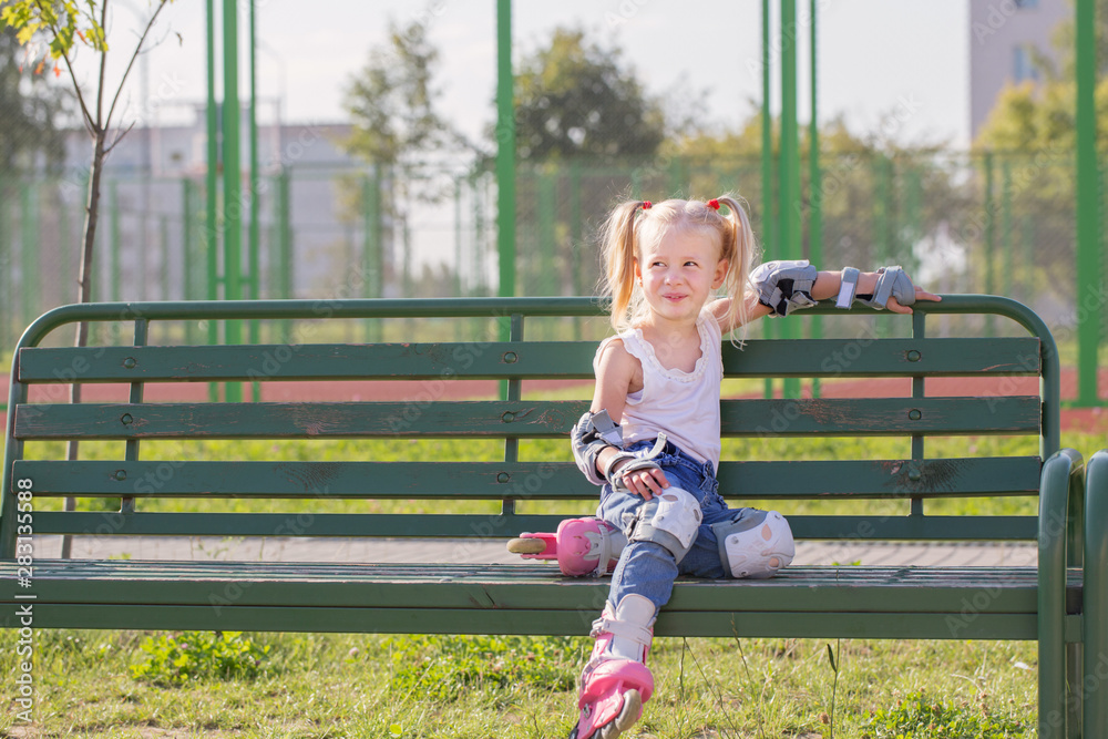little girl sitting on bench in playground in roller skates little girl sitting on bench in playground in roller skates