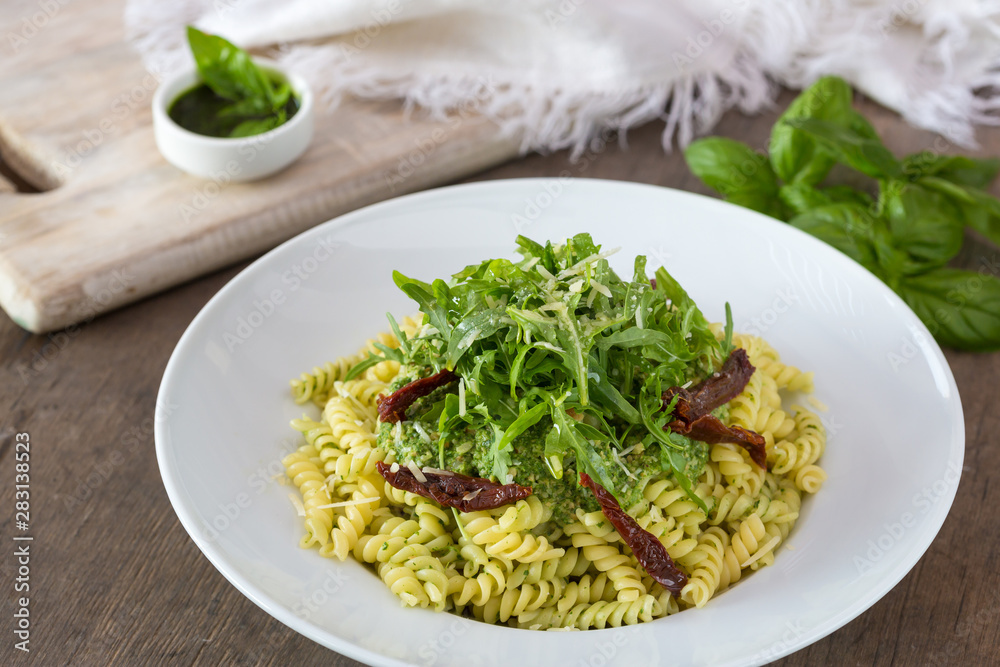 Colored pasta with rukola and basil on white plate with sauce.