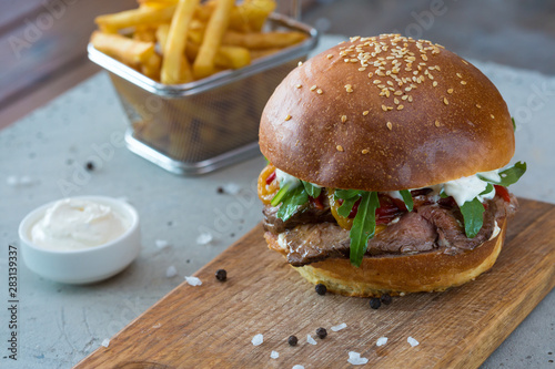 Highigh burger with french fries in small fry basket on concrete surface. Traditional American fastfood.