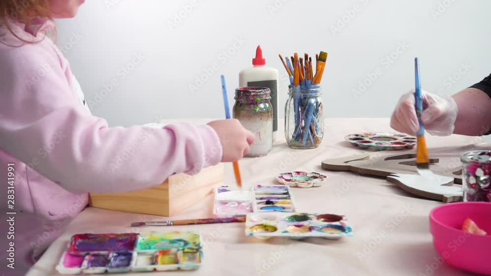 Little girl painting a white unicorn with acrylic paint on a wooden box. Little girl painting a white unicorn with acrylic paint on a wooden box.