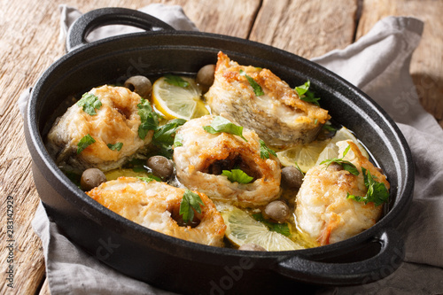 Baked cod fish with lemon and olives in a spicy sauce close-up in a pan. horizontal