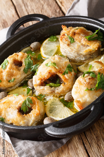 Baked cod steaks with lemon and olives closeup in a pan. vertical