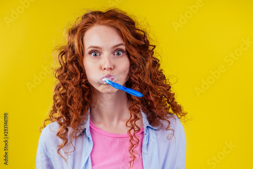 sleepy redhaired ginger woman brushing teeth with toothpaste eco paste on yellow studio background